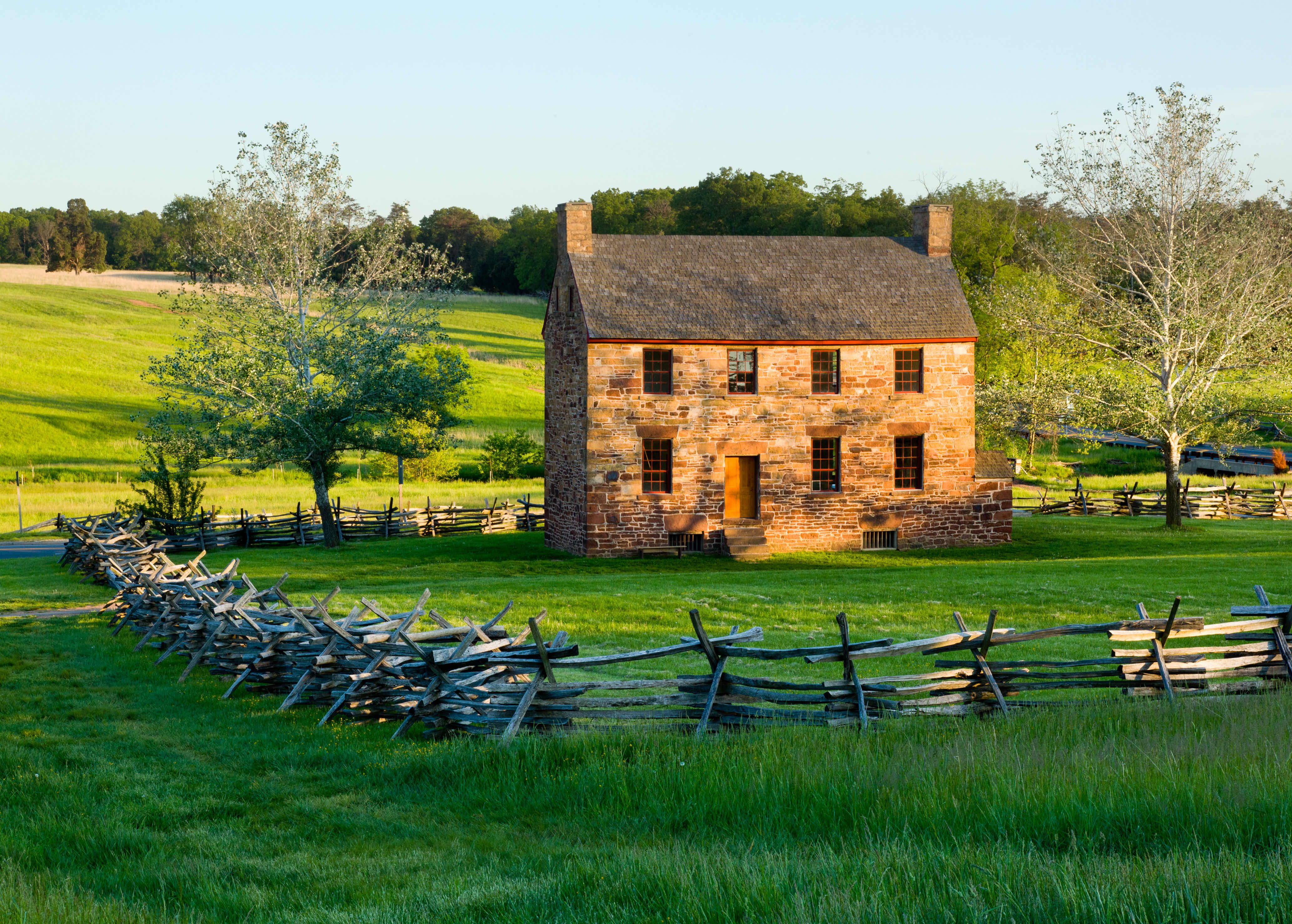 Historic Stone House at Manassas National Battlefield Park in Virginia, surrounded by split-rail fencing and lush green fields at sunset.